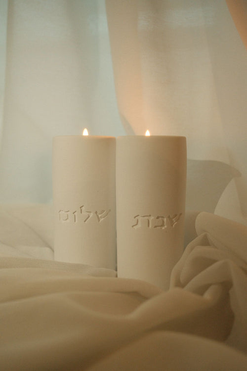 House of Judaica white Shabbat candles with Hebrew lettering in soft fabric setting